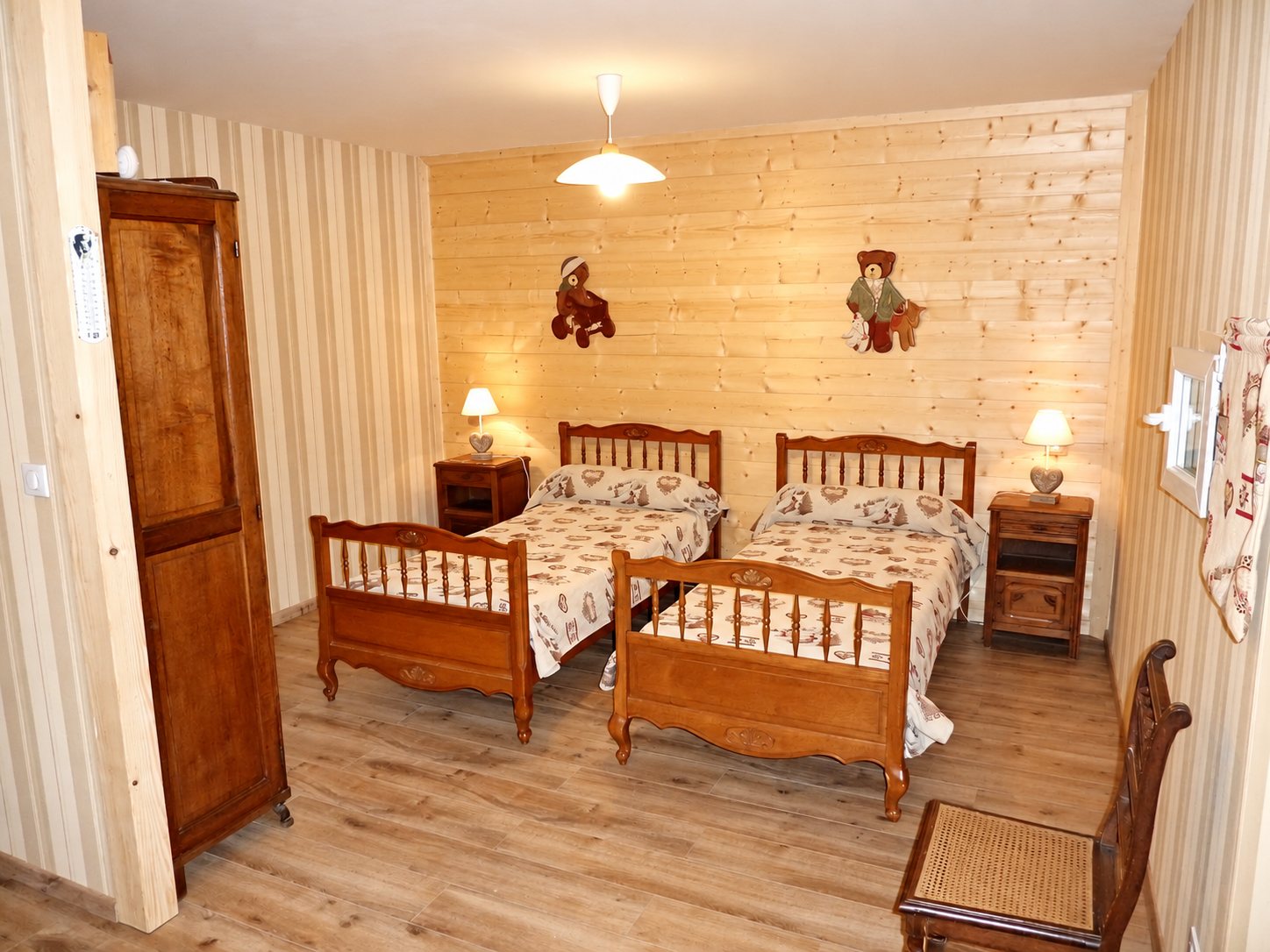 Chambre d'hôtes au décor montagnard avec deux lits jumeaux en bois, deux tables de chevet, une armoire ancienne et des oursons décoratifs sur un mur en lambris clair.