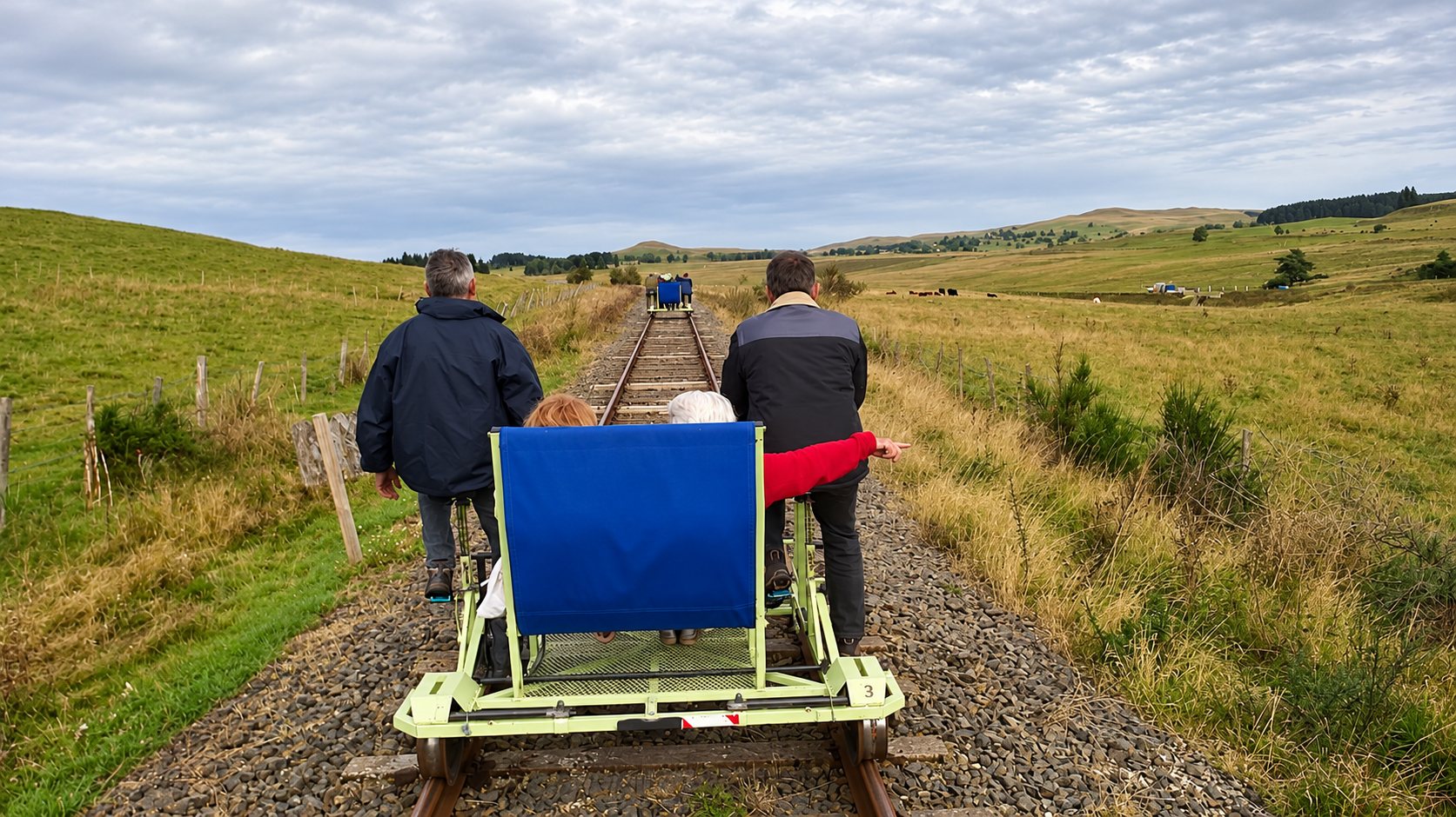 Des passagers voyagent sur une draisine à pédales le long d'une ancienne voie ferrée au milieu de prairies vallonnées.