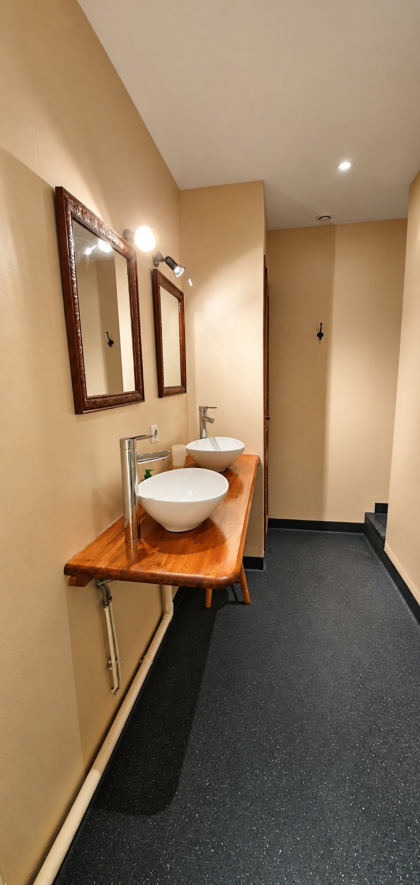 Salle d'eau aux murs beiges avec deux vasques rondes blanches posées sur un plan en bois, deux miroirs encadrés et un sol sombre.