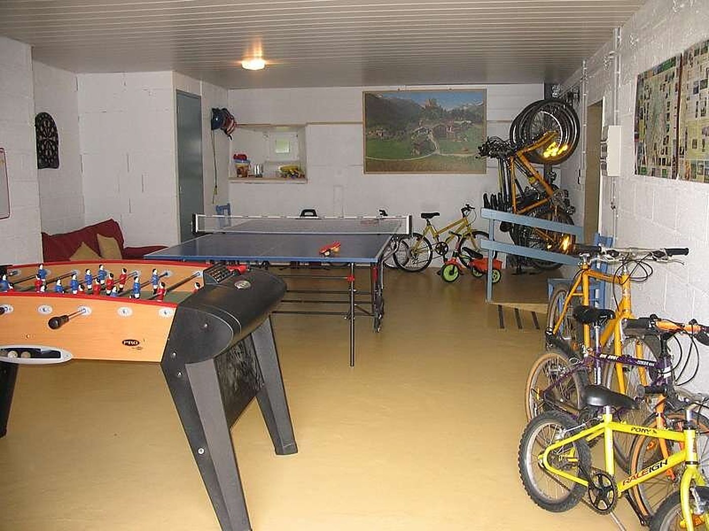 Une salle de jeux au sol jaune avec un baby-foot, une table de ping-pong et plusieurs vélos rangés le long des murs en parpaings.