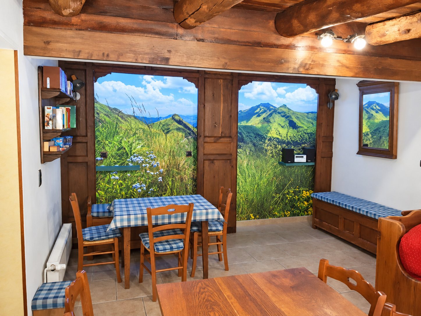 Salle à manger rustique avec poutres en bois, tables dressées de nappes à carreaux bleus et blancs, et une grande fresque murale de montagnes verdoyantes.